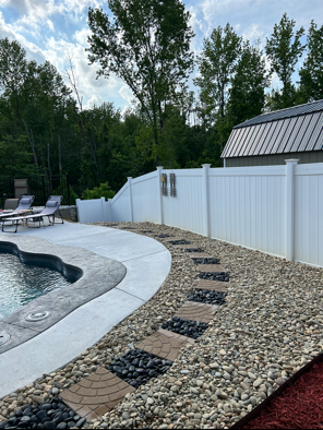 Backyard pool deck with white fence, gravel path, trees, and stone pavers along the water edge