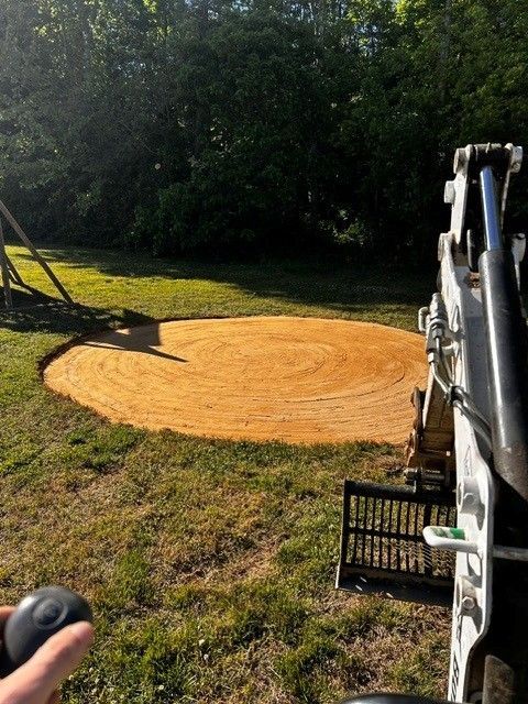 Freshly spread tan mulch circle in a grassy yard beside a piece of landscaping equipment