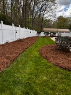 Backyard path with green lawn strip between red mulch beds and a white fence