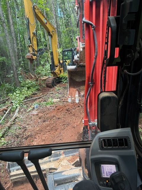 Excavator clearing a muddy forest trail, viewed from inside a red machine cab.