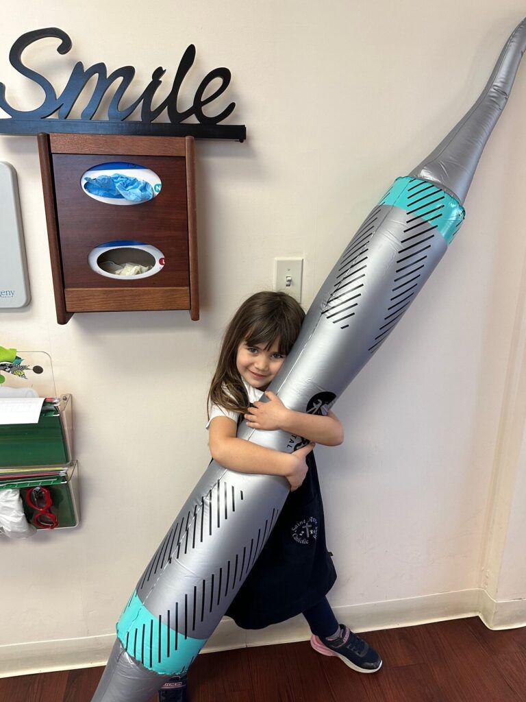 A little girl is holding an inflatable toothbrush in a dental office.