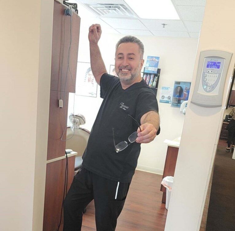 A dentist is standing in a dental office with his fist in the air.