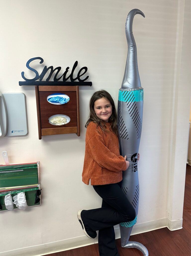 A young girl is standing next to a large inflatable toothbrush in a dental office.