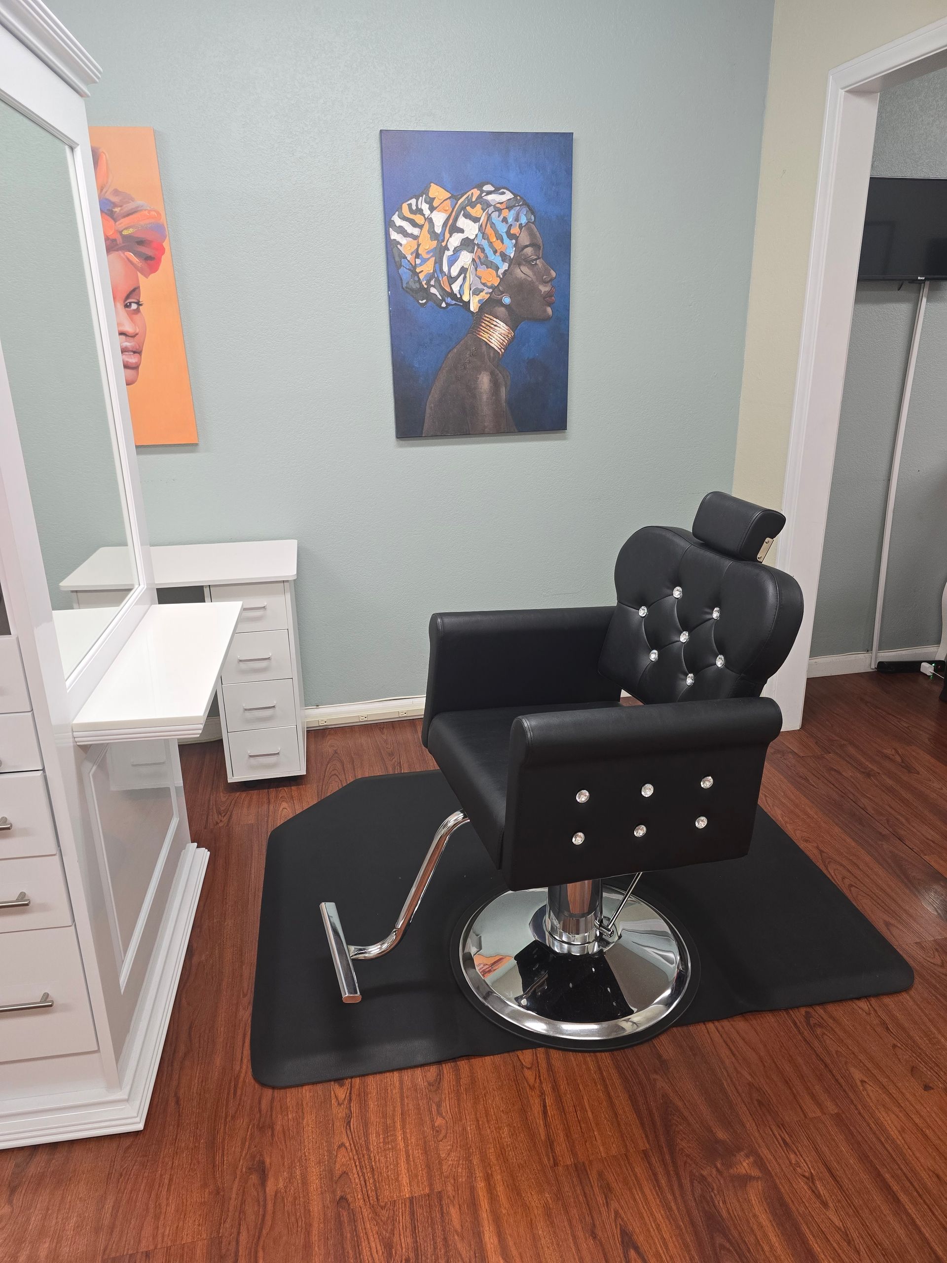 A black hair salon chair is in a room with a painting on the wall