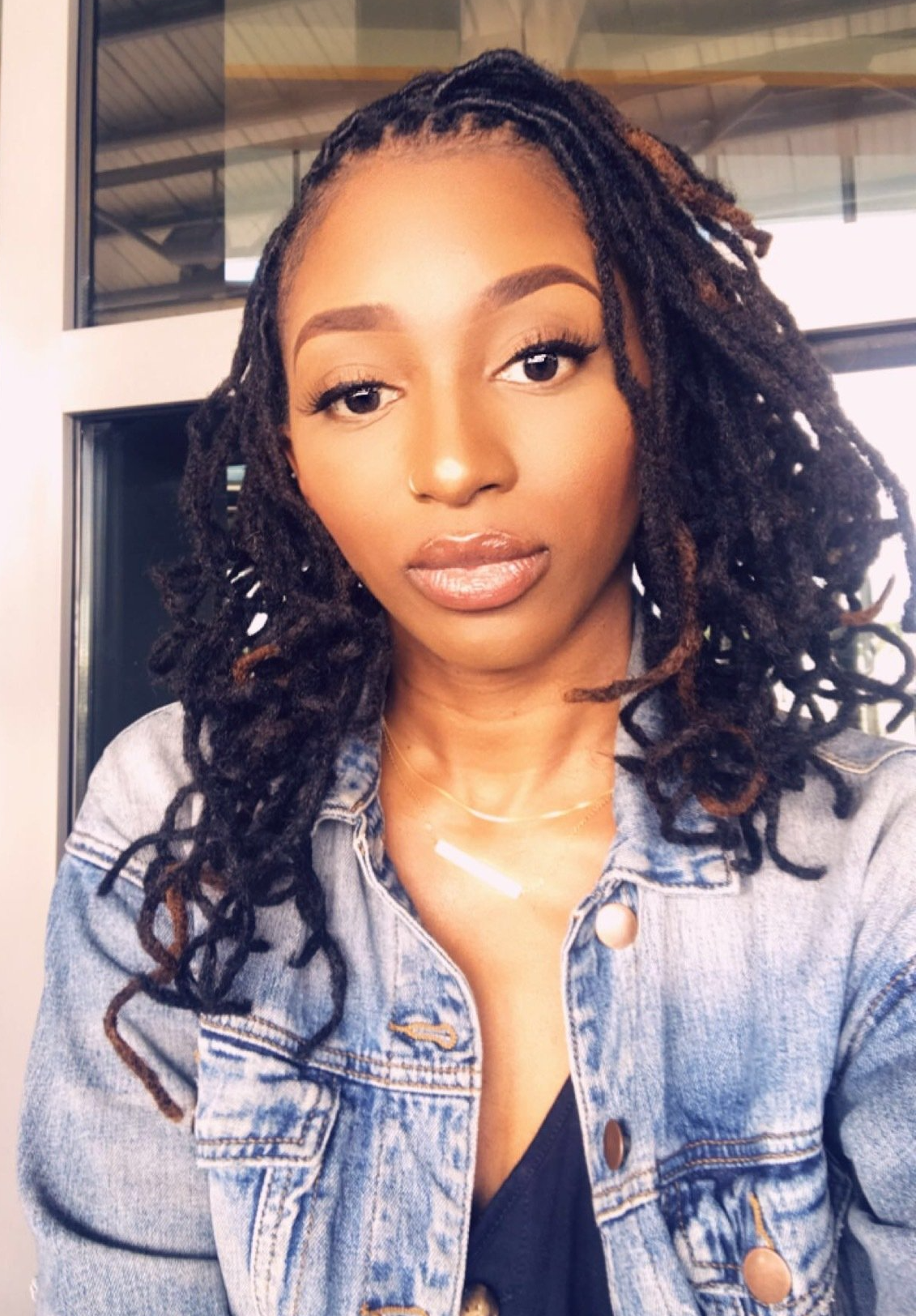 A woman with dreadlocks is wearing a denim jacket and a black top.