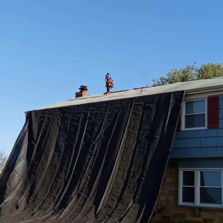 A man is standing on top of a roof with a tarp on it