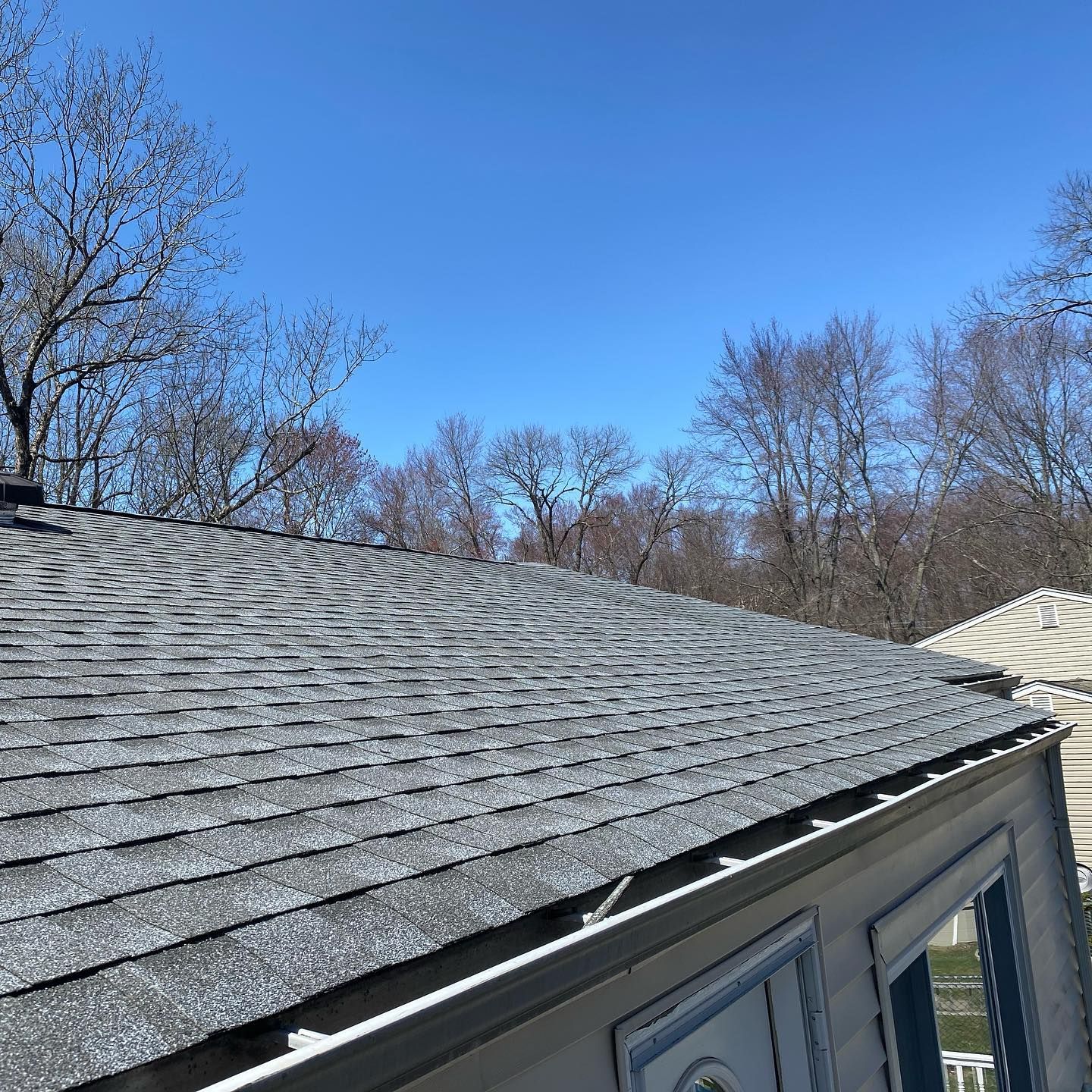 A roof of a house with a blue sky and trees in the background