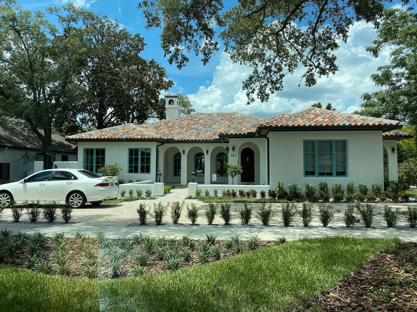 A white car is parked in front of a white house