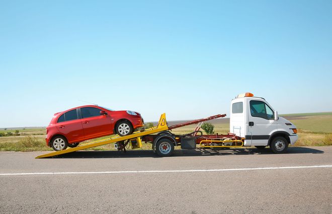 Red car on a tow truck on a highway under a clear blue sky.