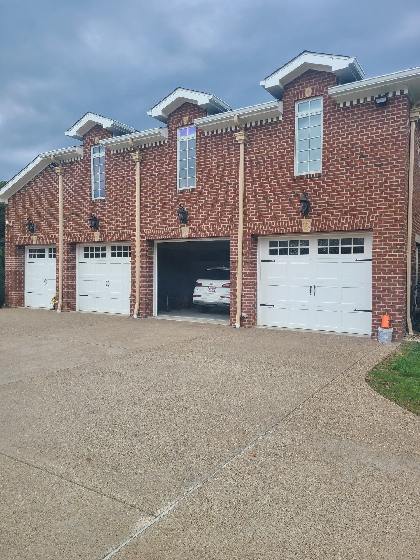 Brick apartment garages with one open bay and a wet driveway under overcast skies