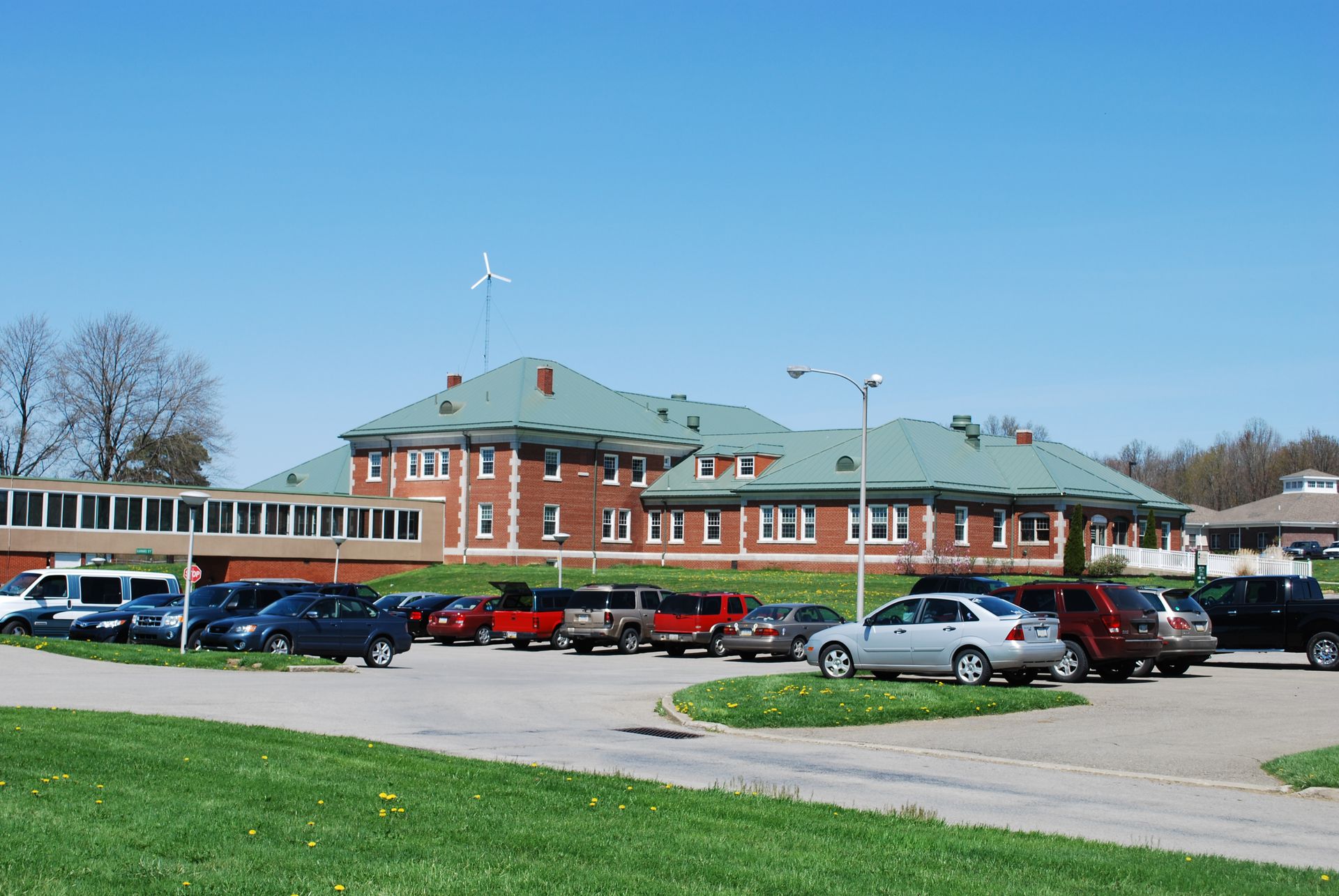 Historic brick building with green roof and parking lot under a clear blue sky