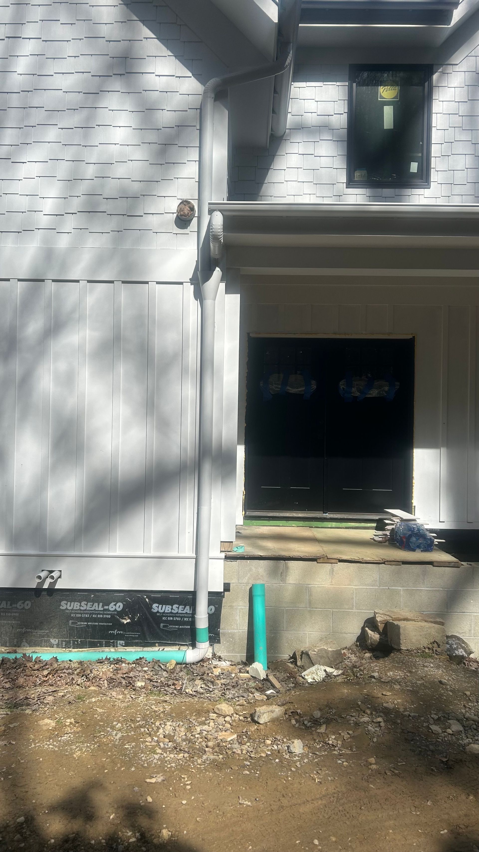 Front of a house under construction with white siding, black door, and dirt yard in the foreground