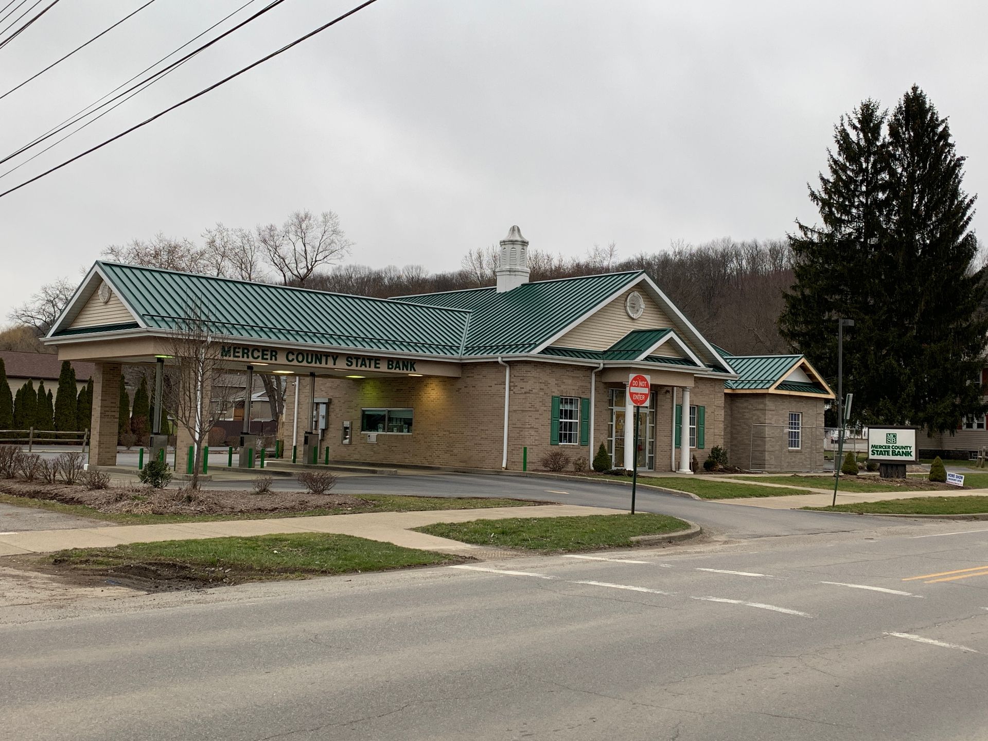 Small roadside building with green roof and covered drive-through lane on a cloudy day.