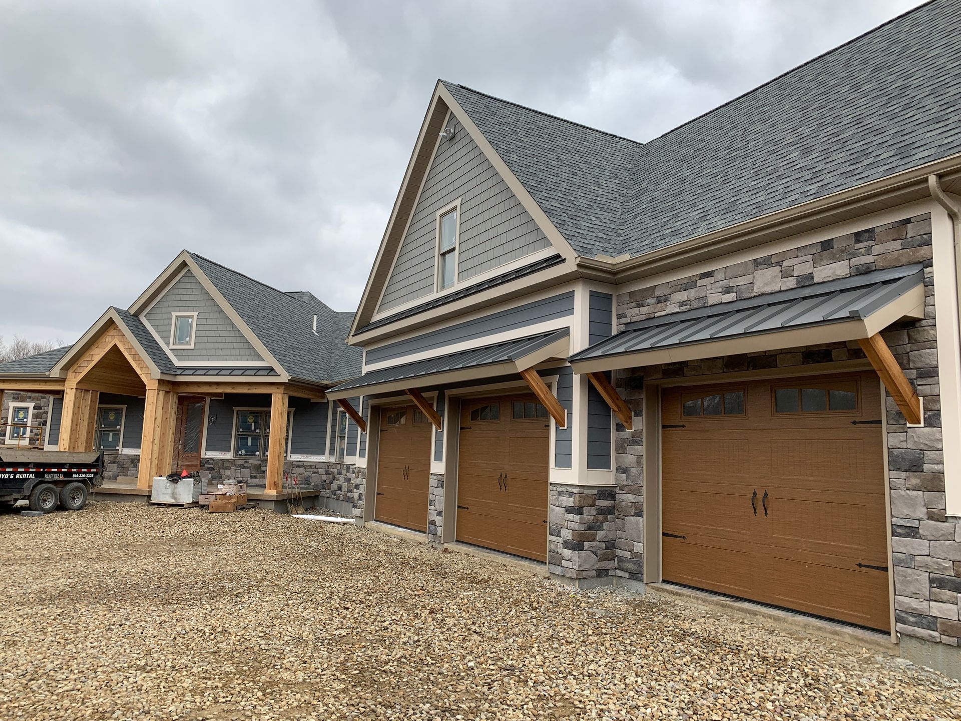 Row of new stone-and-wood garage doors with gabled roofs on a gravel driveway
