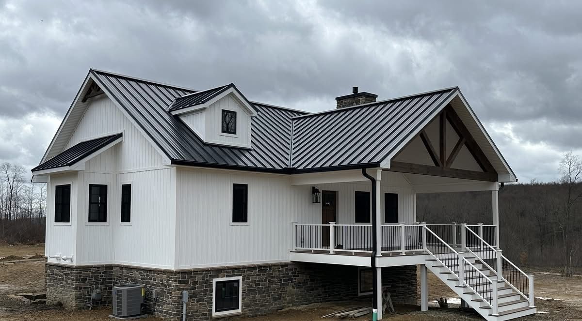 White house with dark metal roof and front porch on a rural lot under cloudy sky
