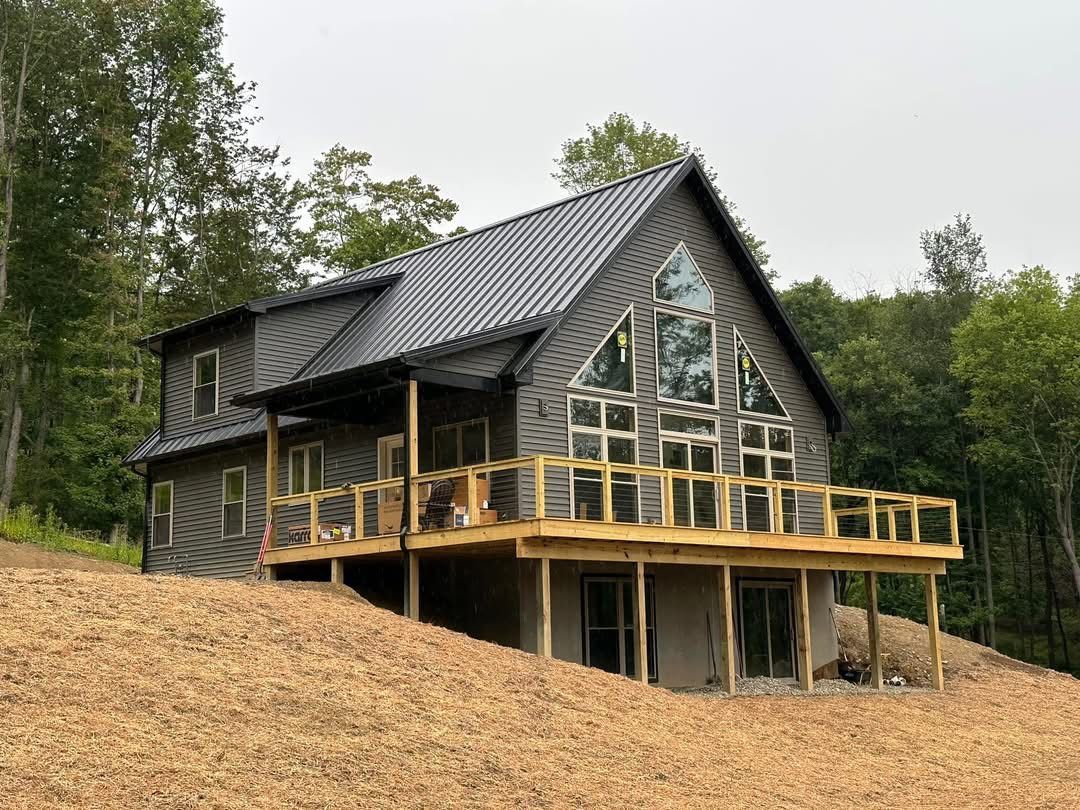 Modern cabin with dark metal roof, wood deck, and large windows on a wooded hillside