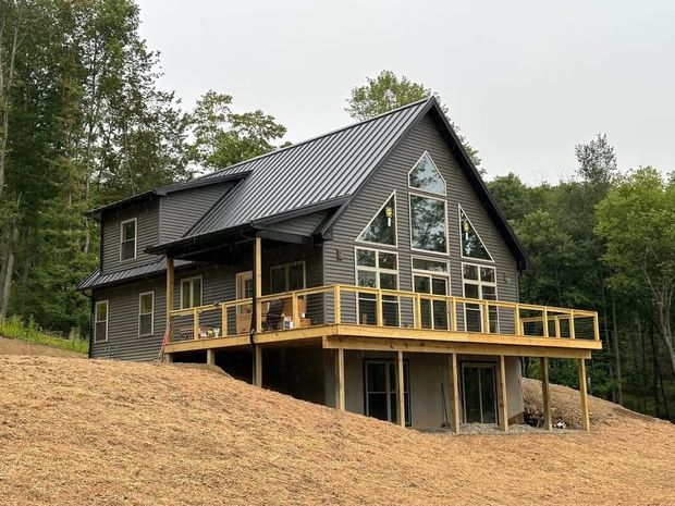 Modern cabin with dark roof and wooden deck on a grassy hillside surrounded by trees