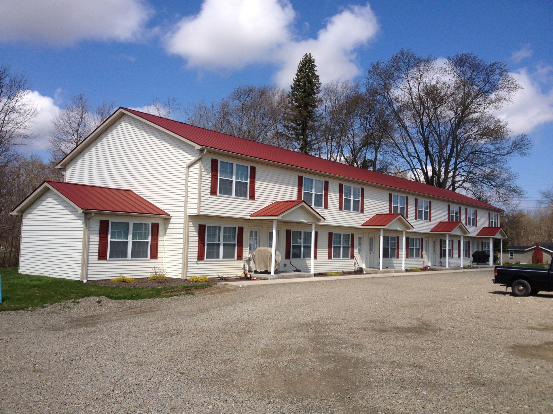 White two-story motel with red roof and trim on a gravel lot under a blue sky