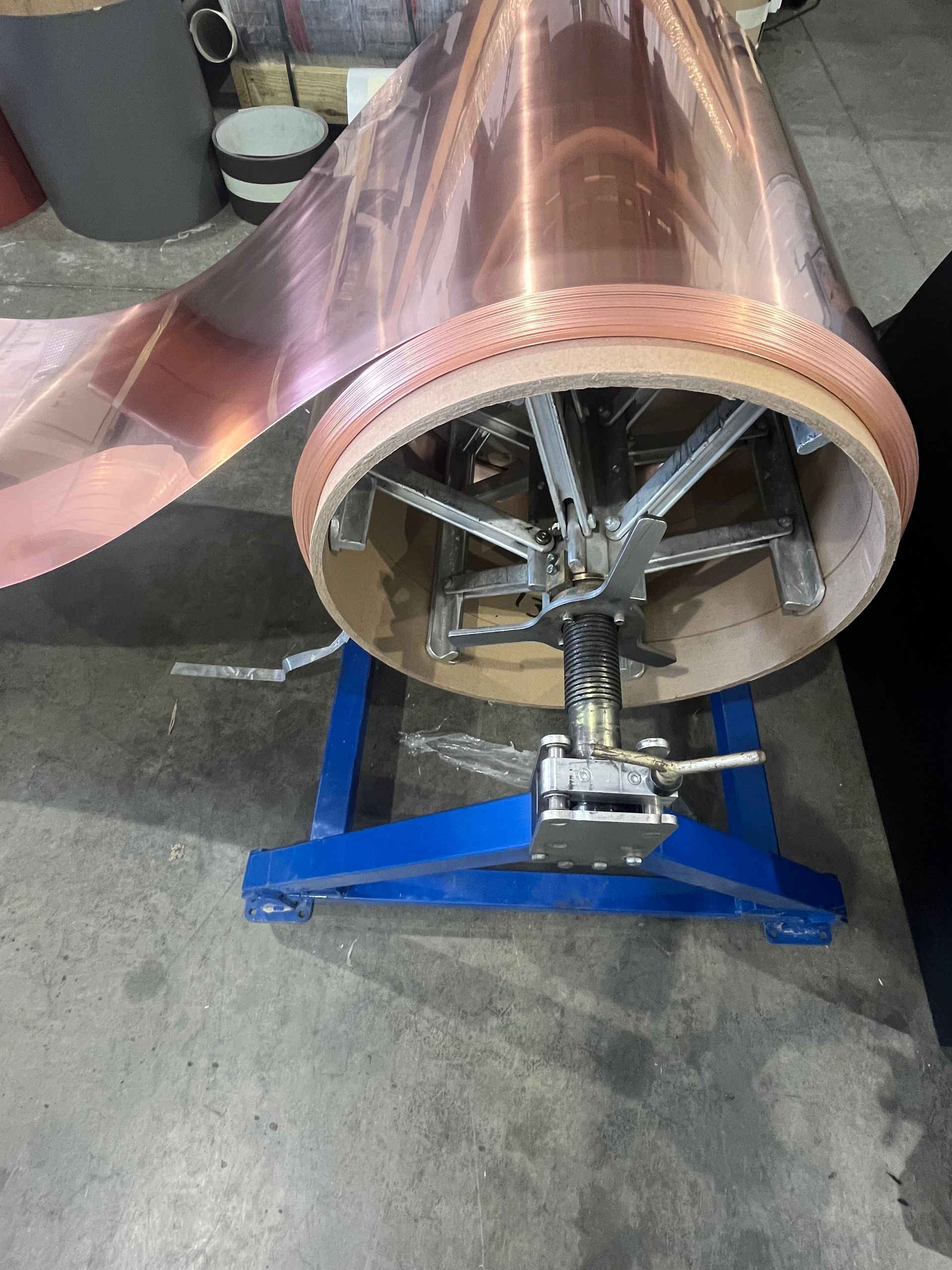 Copper coil or drum on a blue stand in a workshop, with a metal wheel inside the open end.