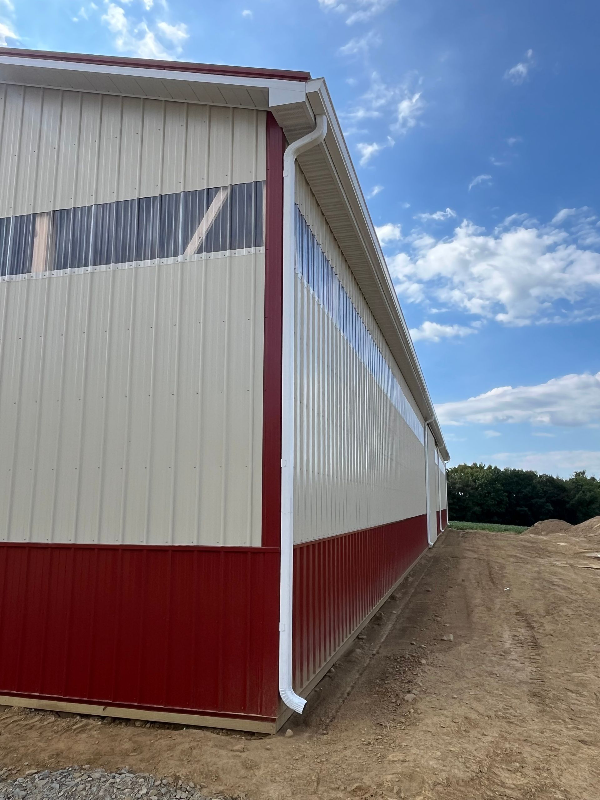 Long white and red metal building along a dirt path under a blue sky