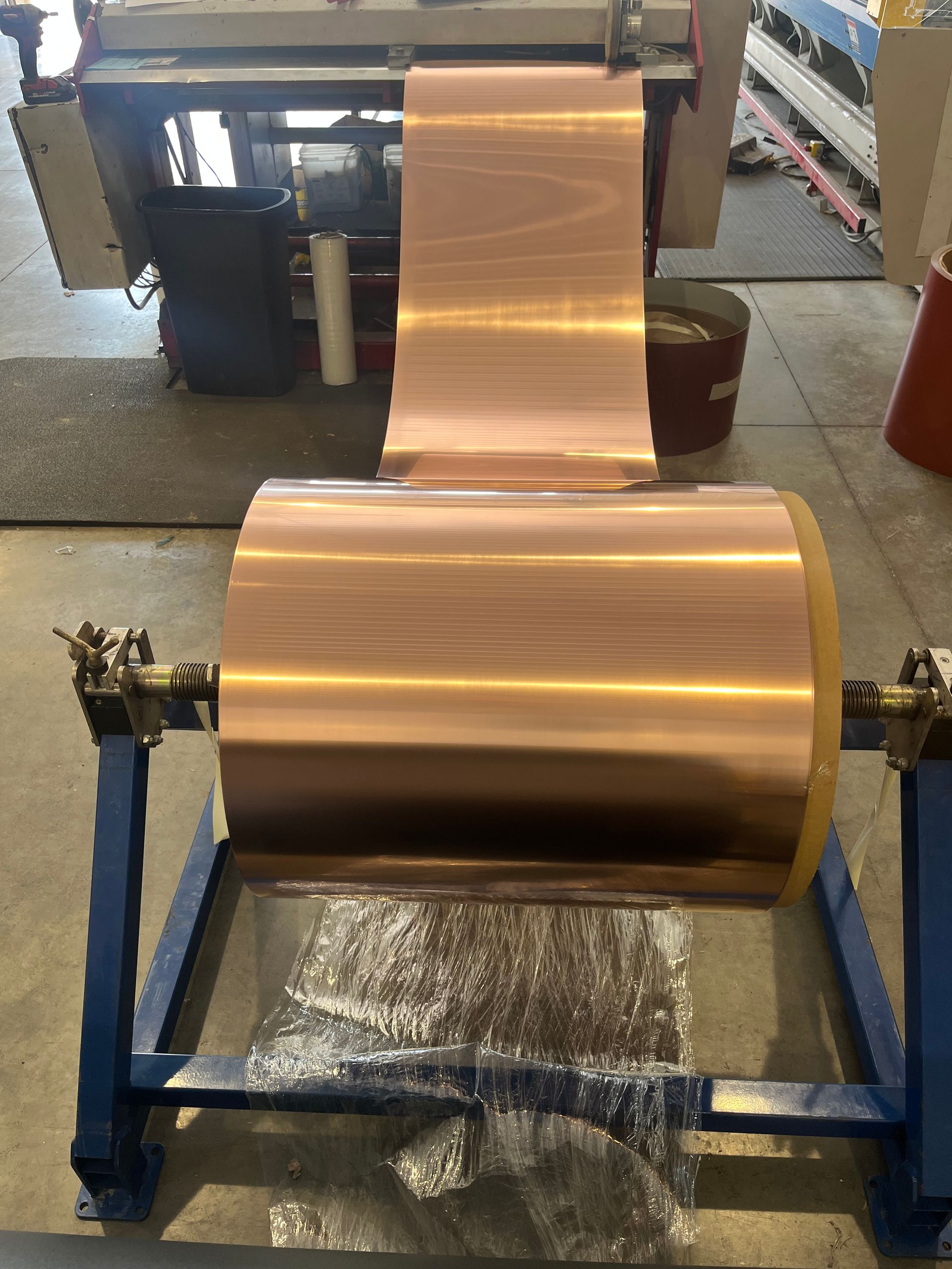 Copper-colored metal sheet on a rolling machine in an industrial workshop.