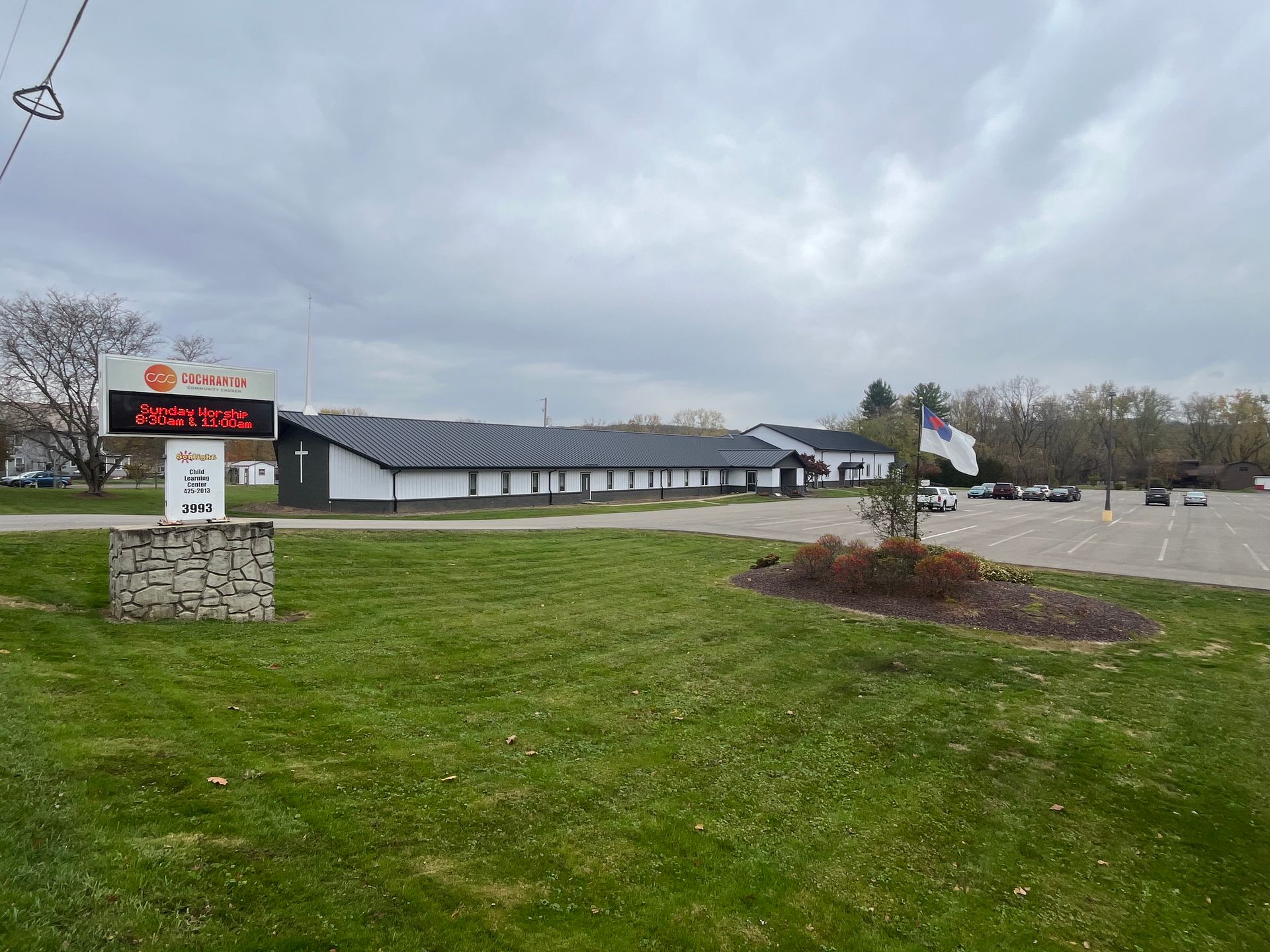Low building and roadside digital sign beside a grassy lot under a cloudy sky