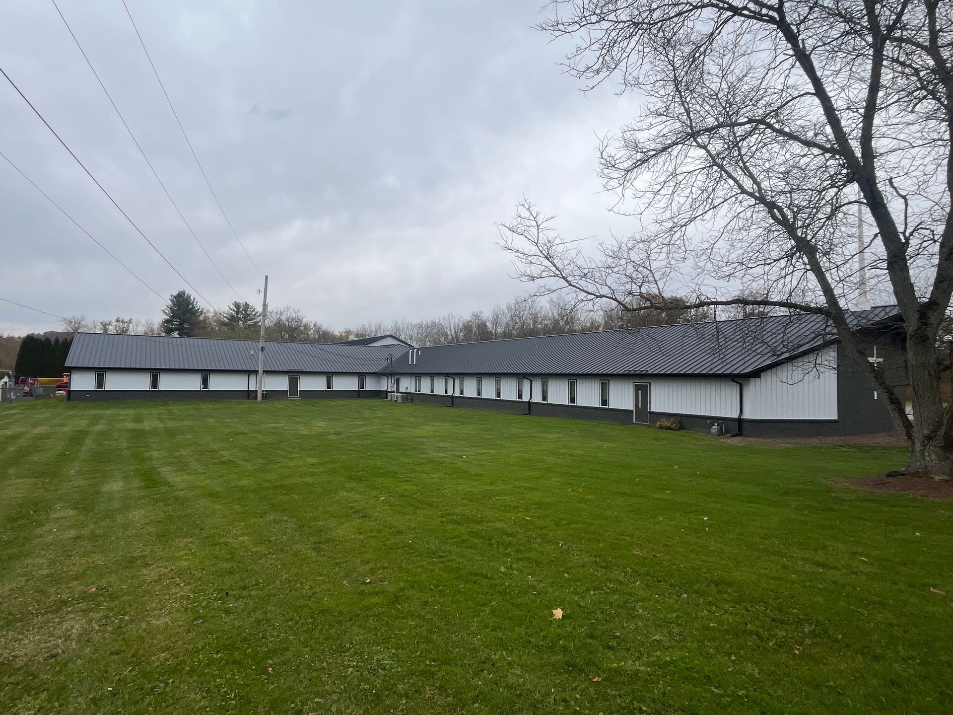 Long white building with a black roof on a grassy field under an overcast sky