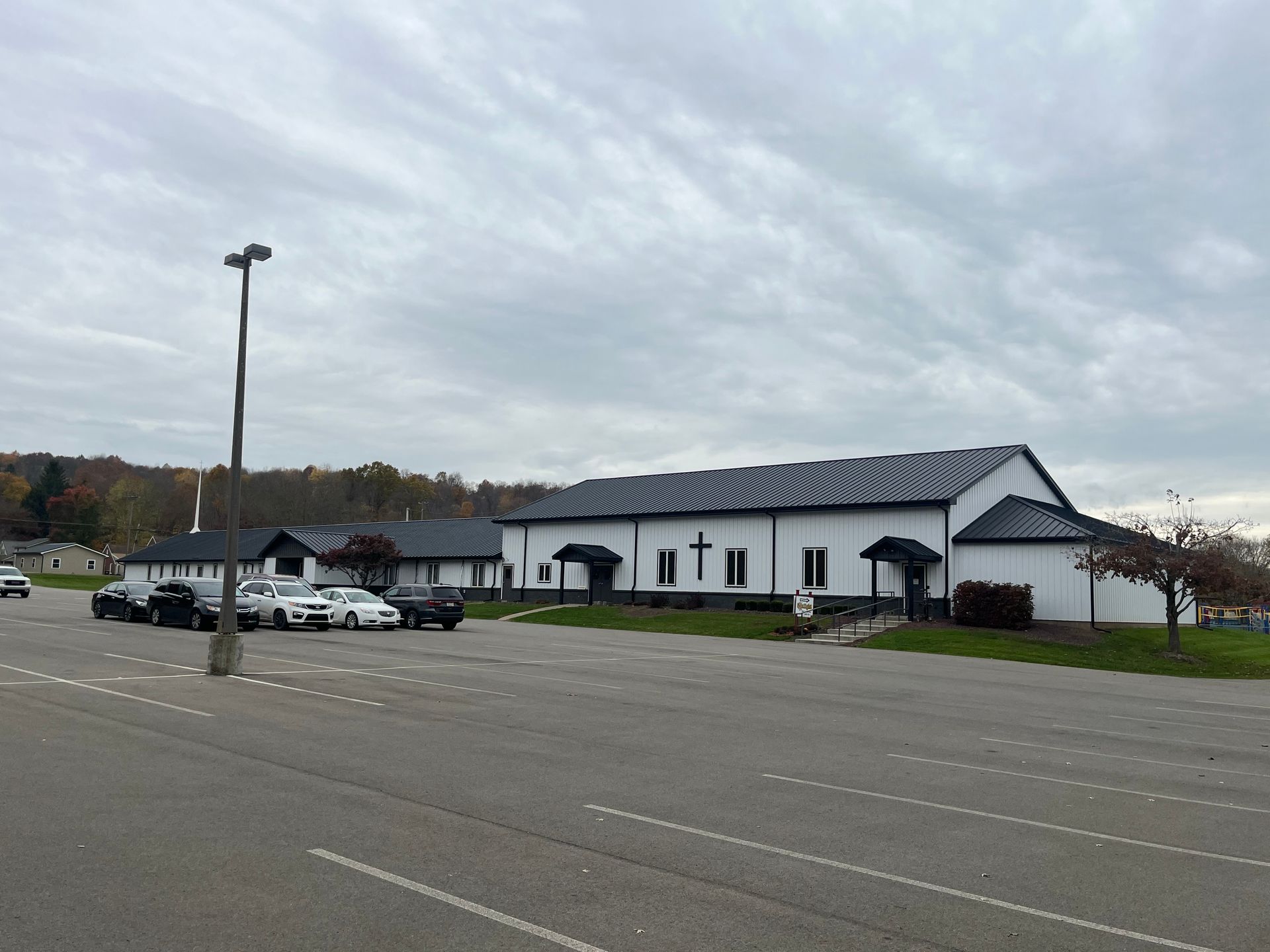 Parking lot beside a white church-like building under a cloudy sky, with a few cars parked nearby.