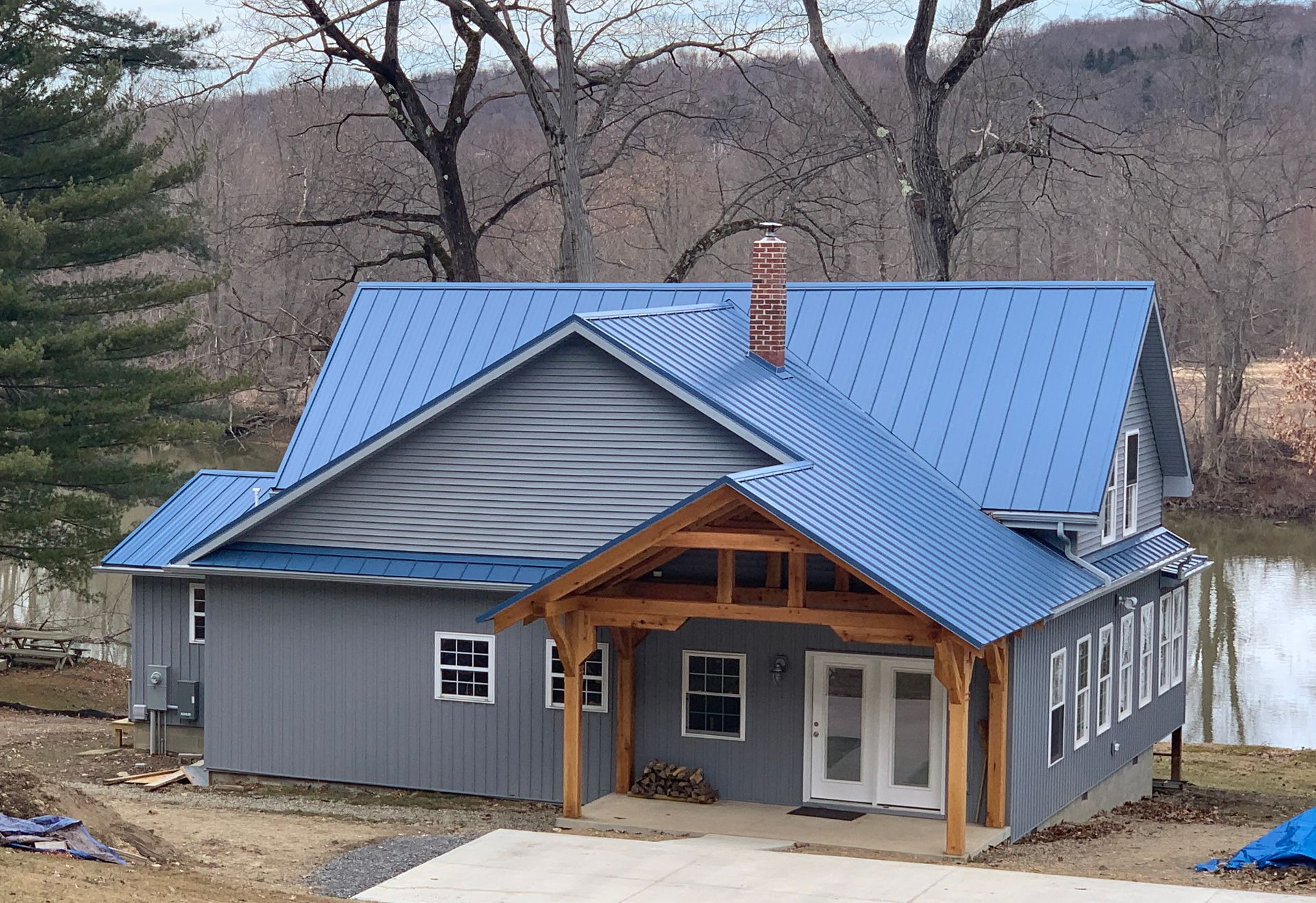 Gray house with blue metal roof and wood porch in a wooded rural setting
