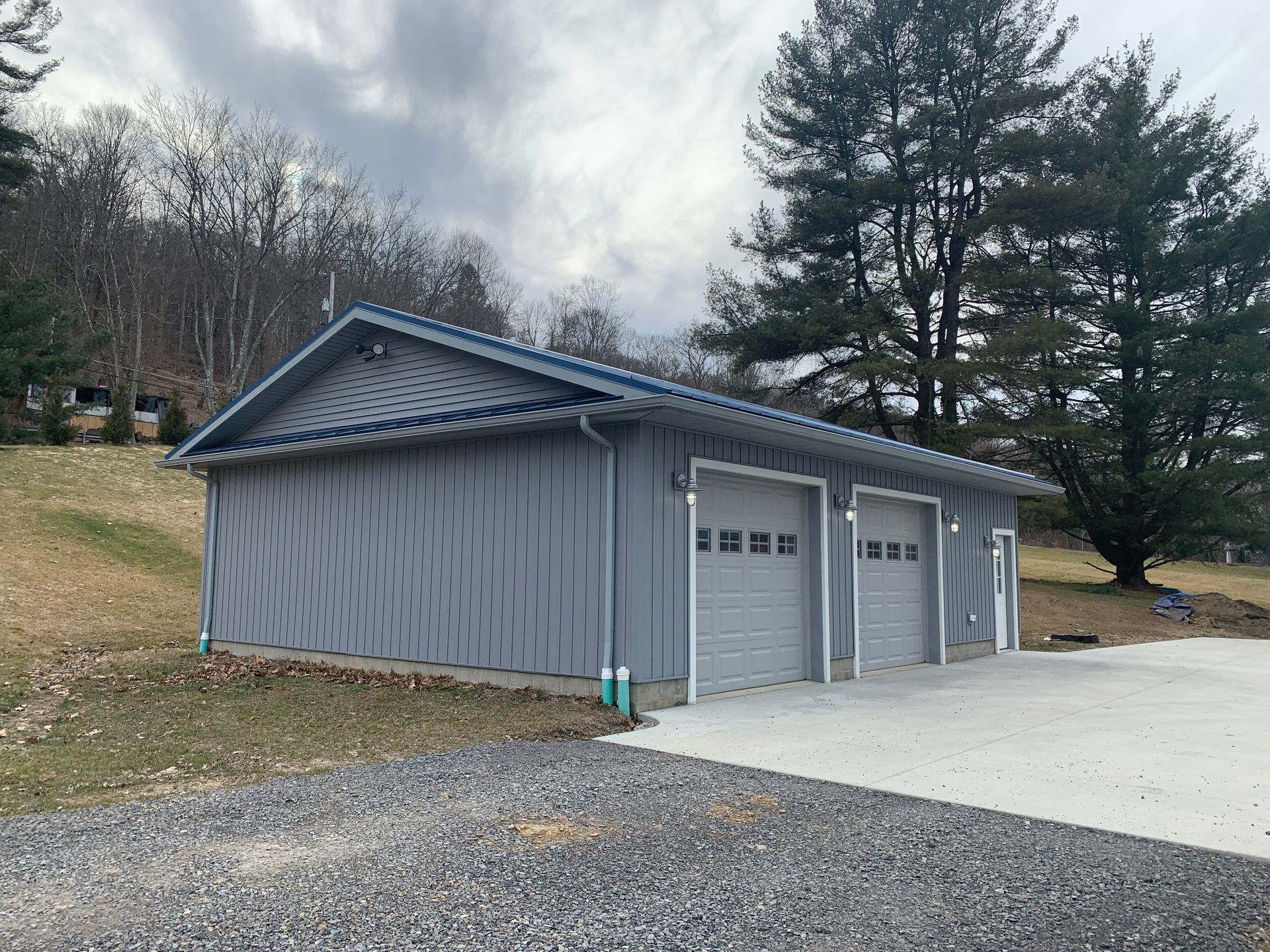 Gray detached garage with two doors and a small side door beside a driveway, under cloudy skies.