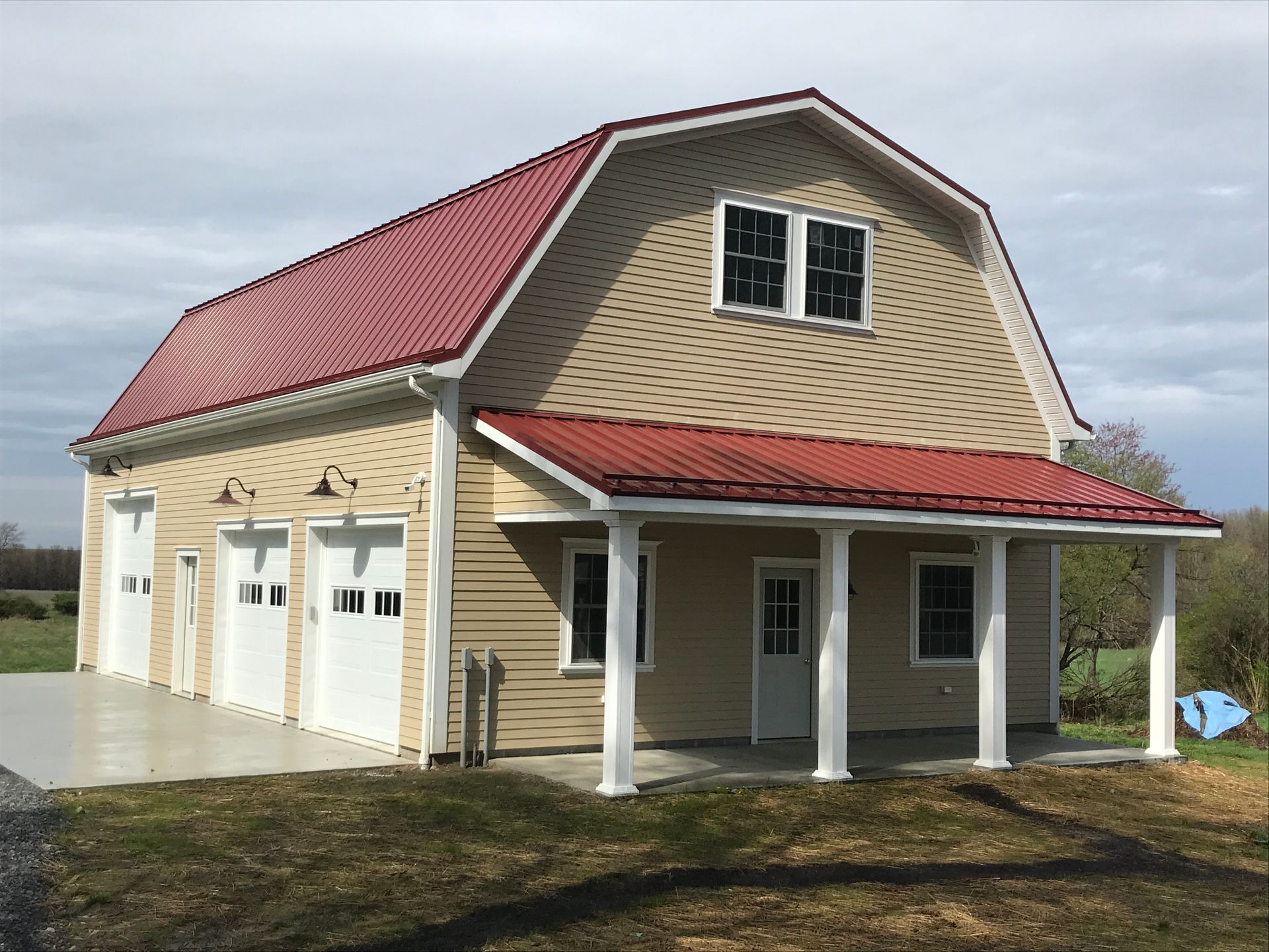 Two-story beige house with red roof, front porch, and garage on a cloudy day