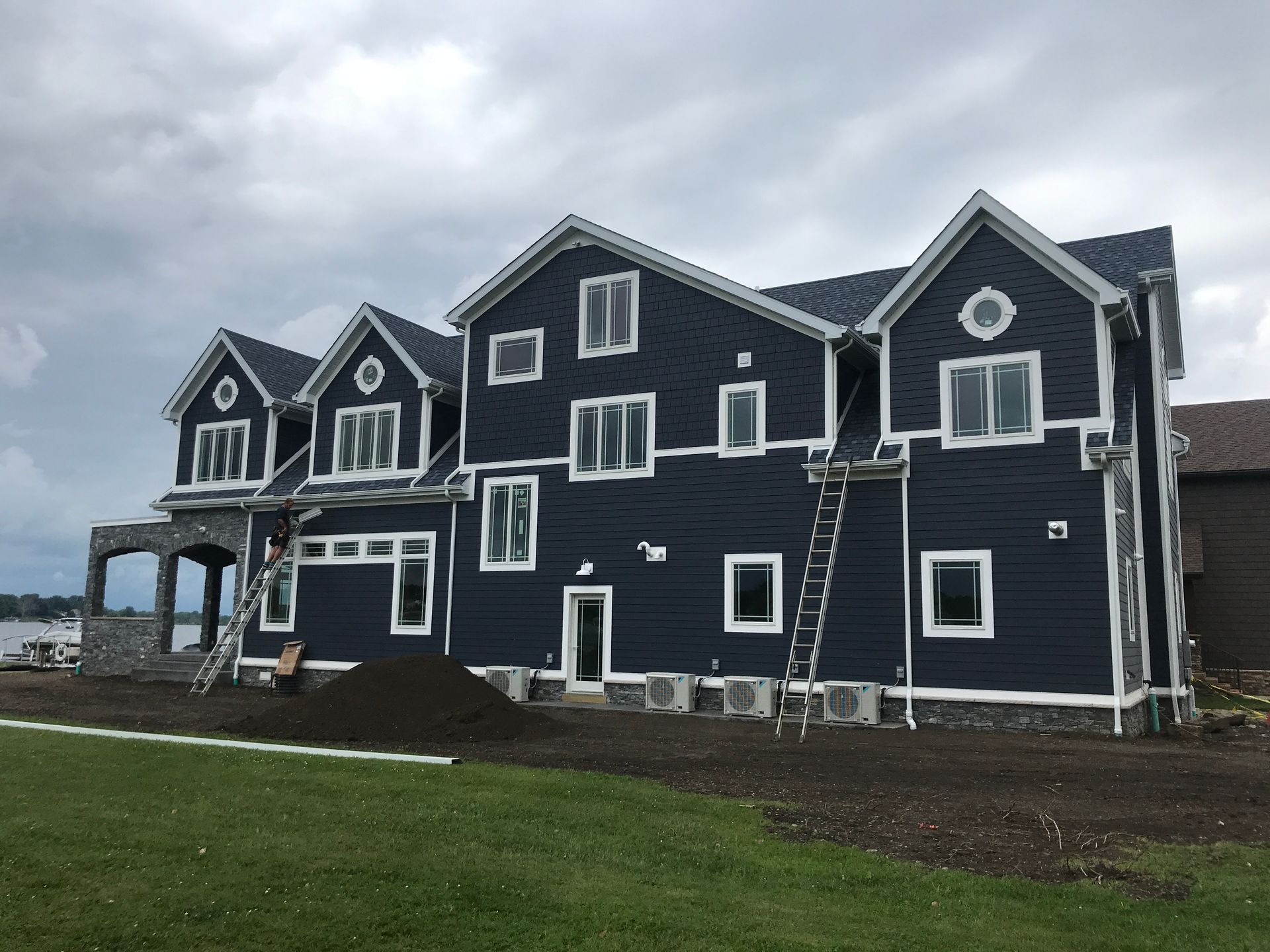 Large dark-blue house with white trim and multiple gables on a grassy lot, viewed from outside during overcast weather