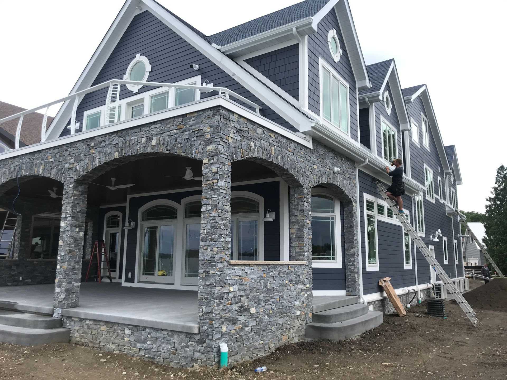 Large gray stone house with white trim, covered porch, and dormer windows under construction