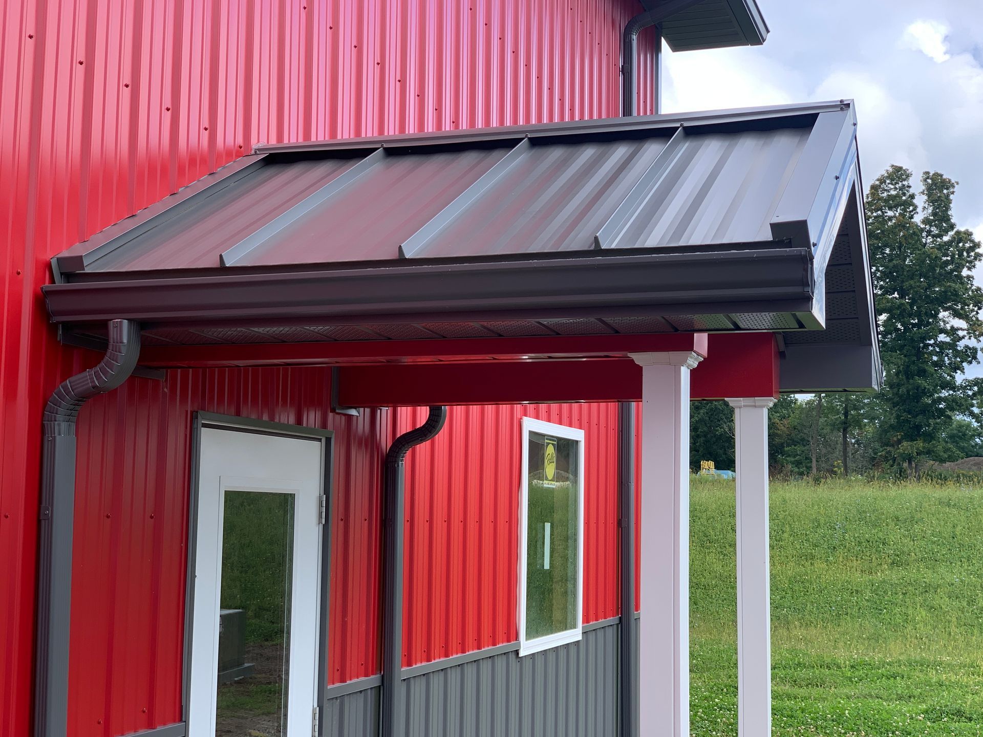 Red metal building entrance with dark awning, white trim, and two windows under overcast sky