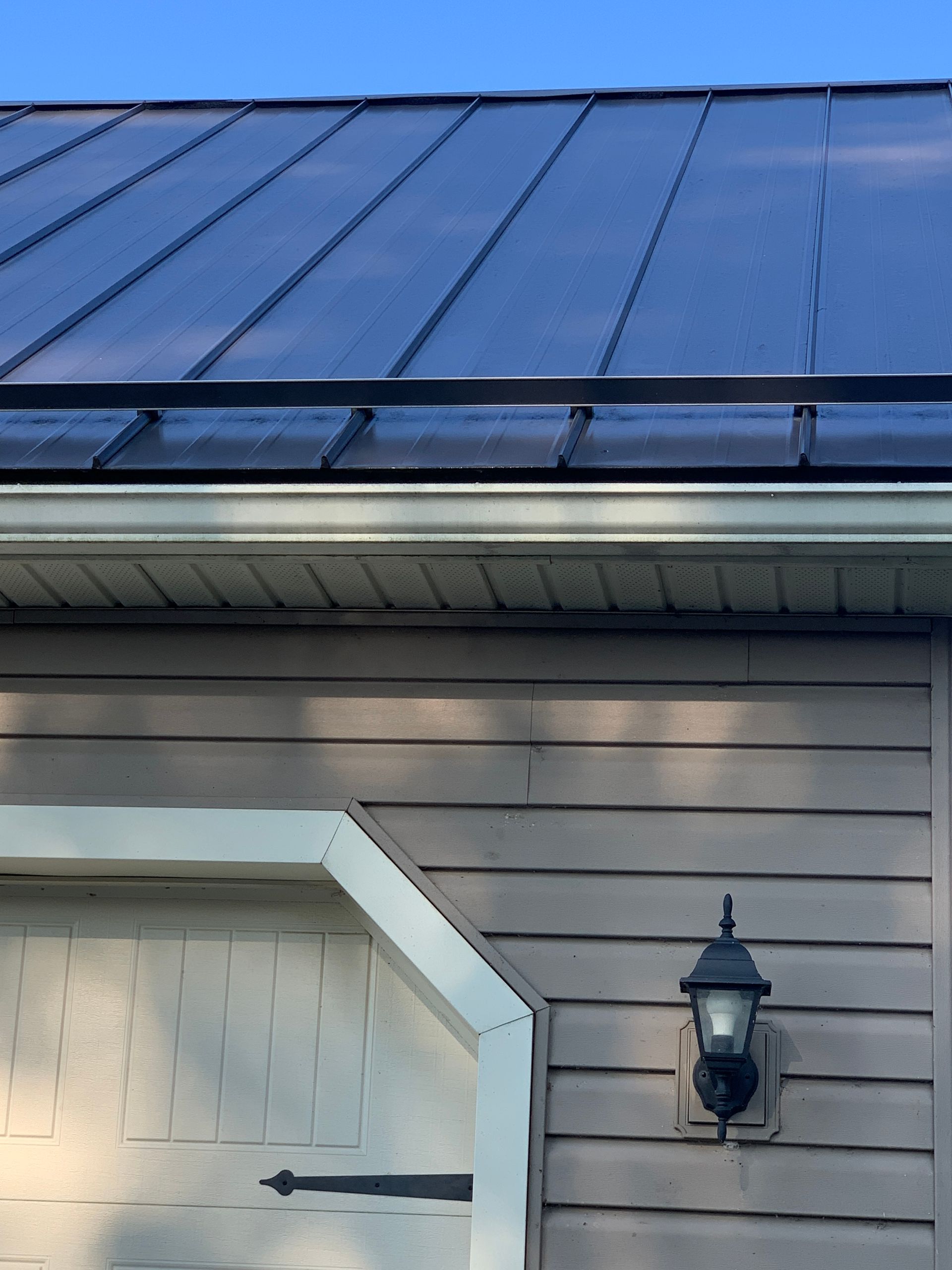 Blue metal roof above gray house siding with a white garage door and black lantern light