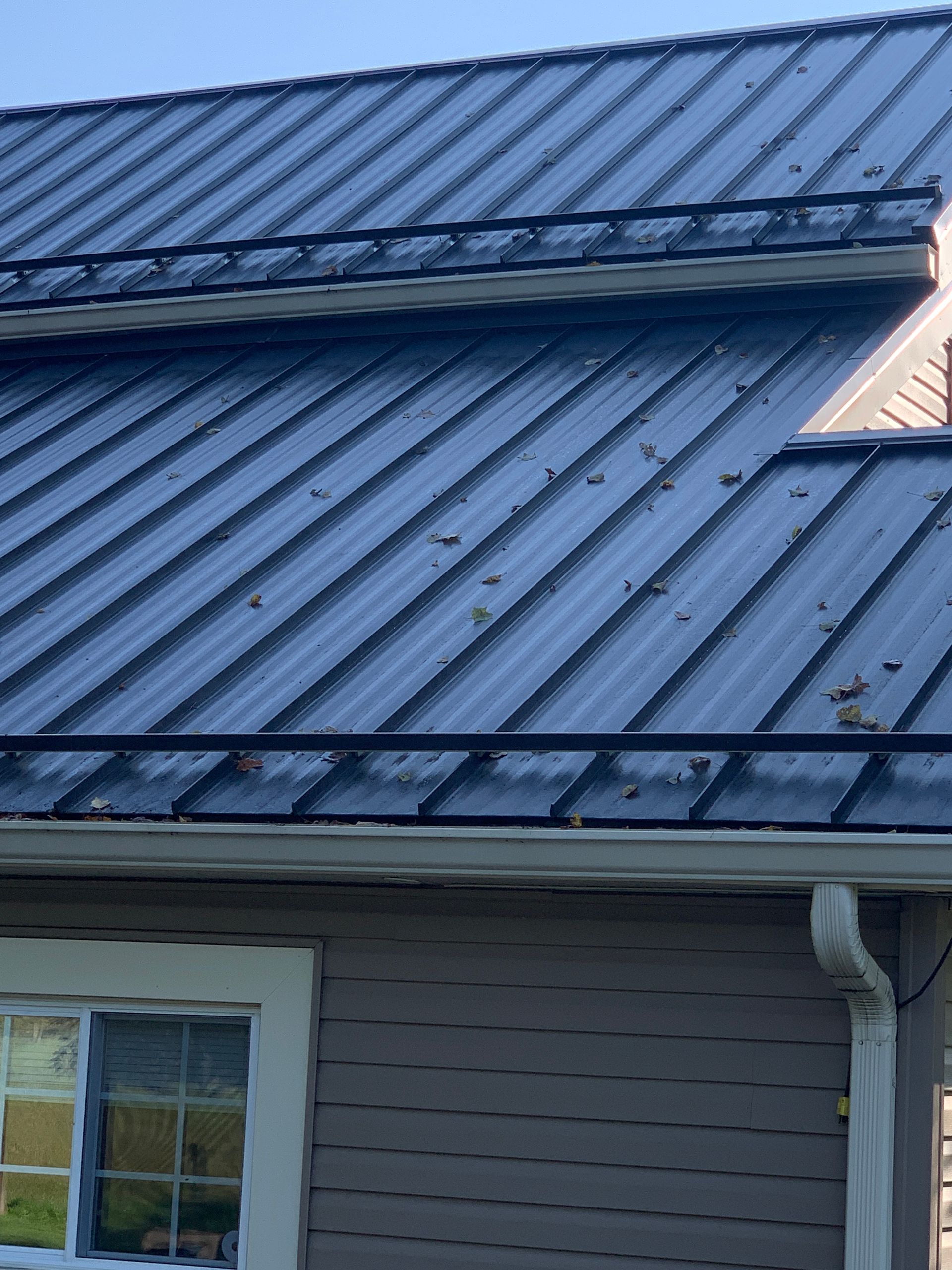Blue metal roof with dormer window and gutter on a house exterior