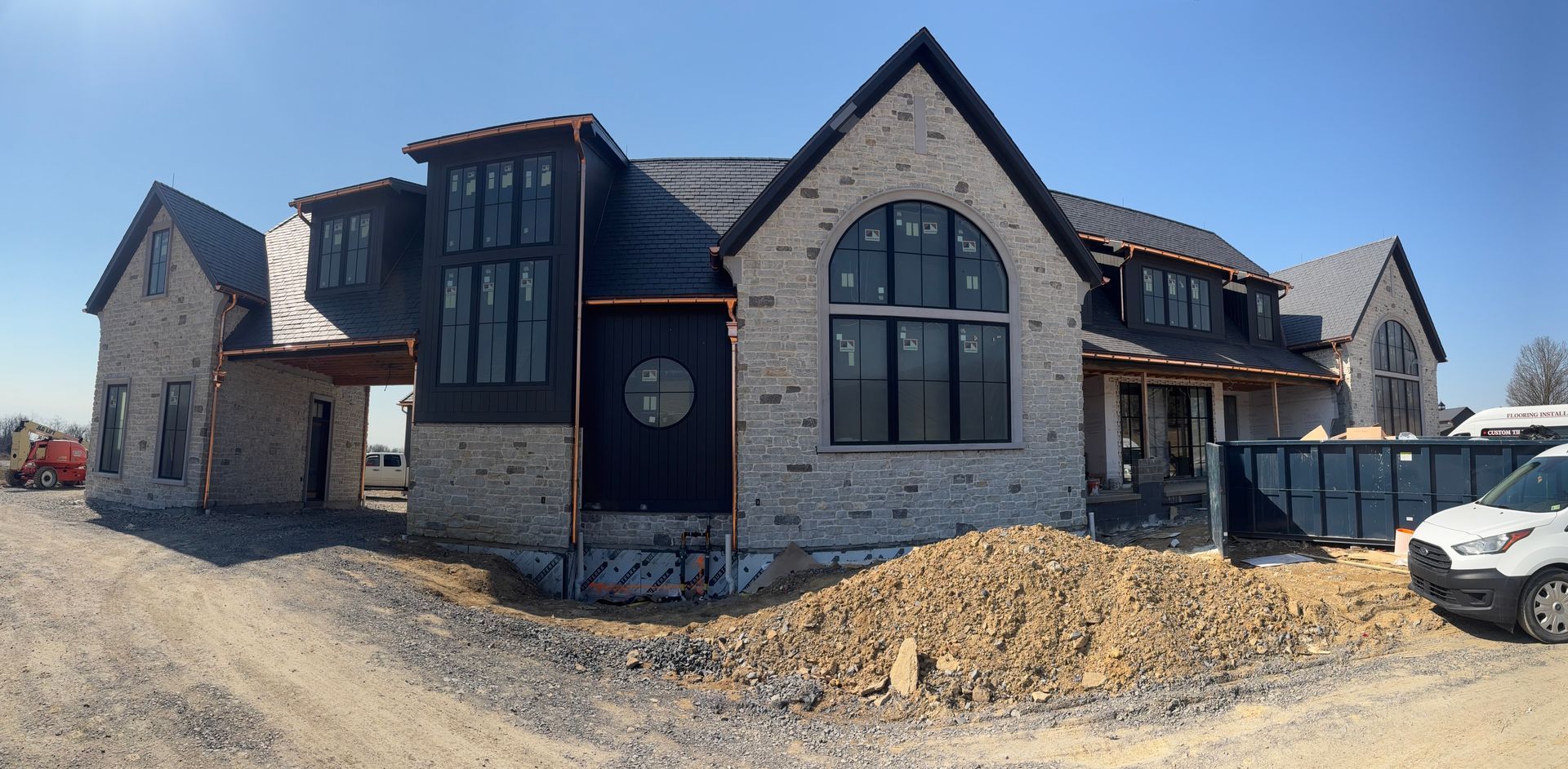 Stone house under construction with black-framed windows and a dirt lot in front