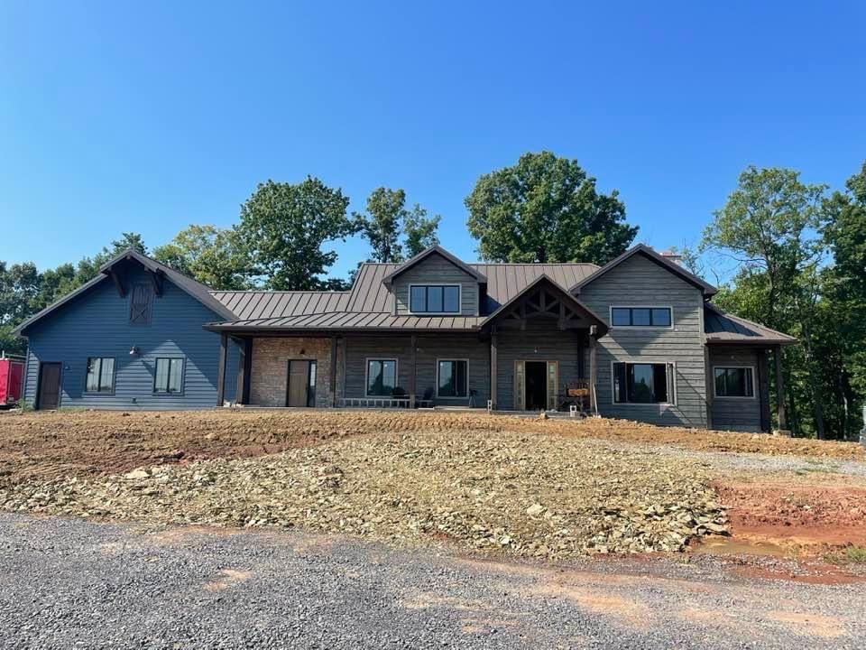 Large gray and stone house under construction on a rocky lot with blue sky and trees