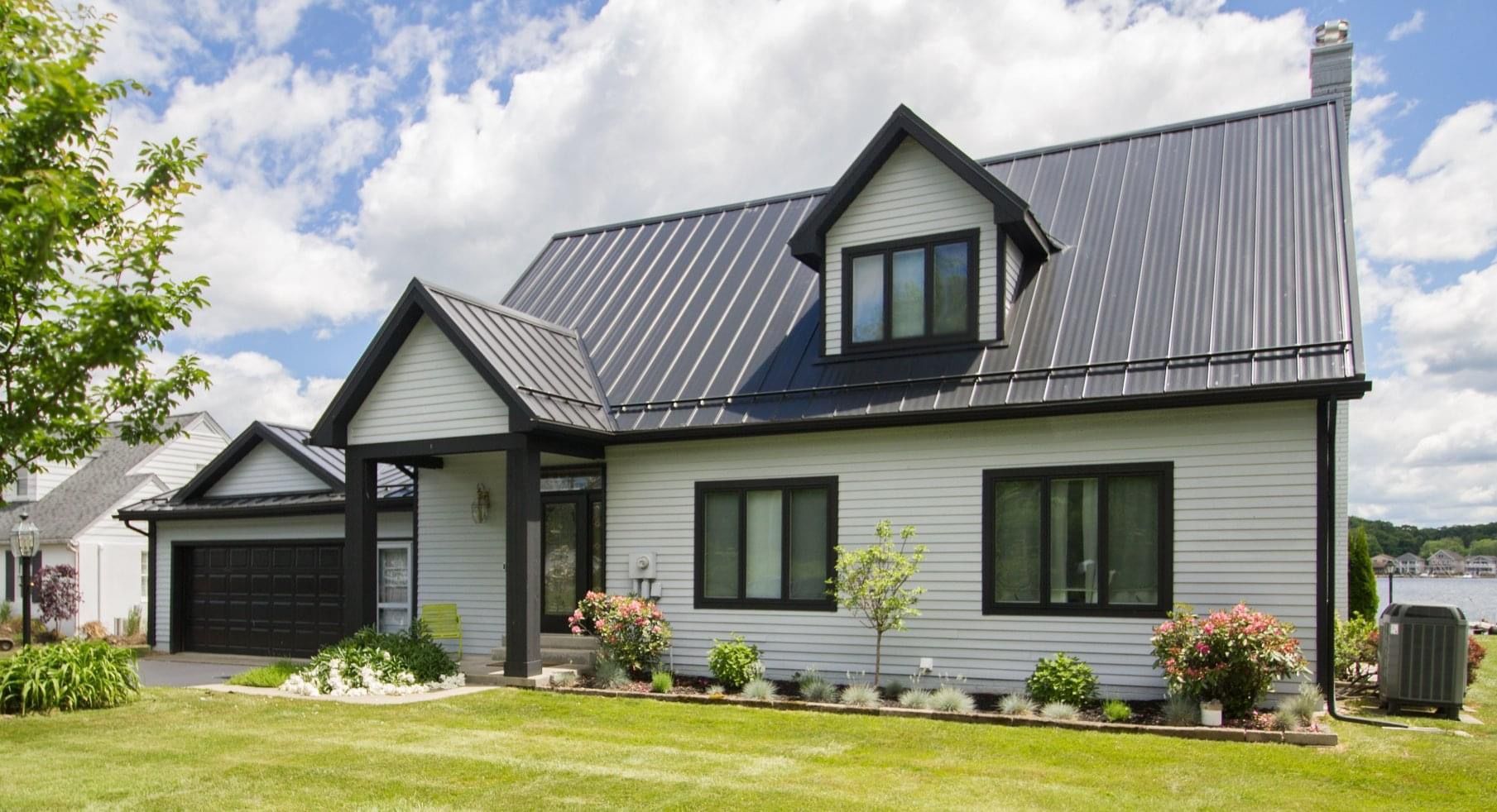 Modern white house with black roof, dormer windows, and attached garage under a partly cloudy sky
