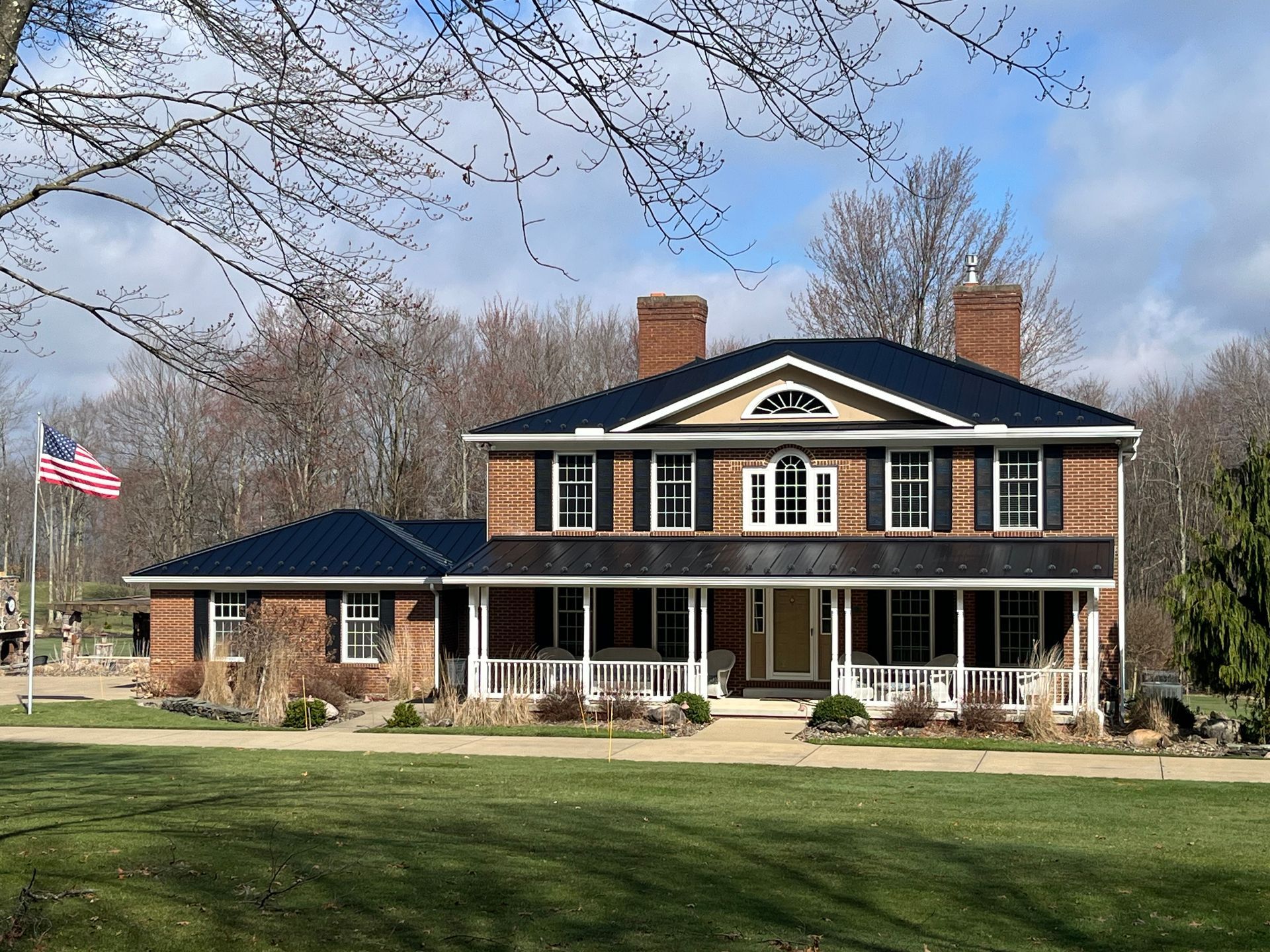 Large brick colonial house with white columns, black roof, and an American flag on a lawn