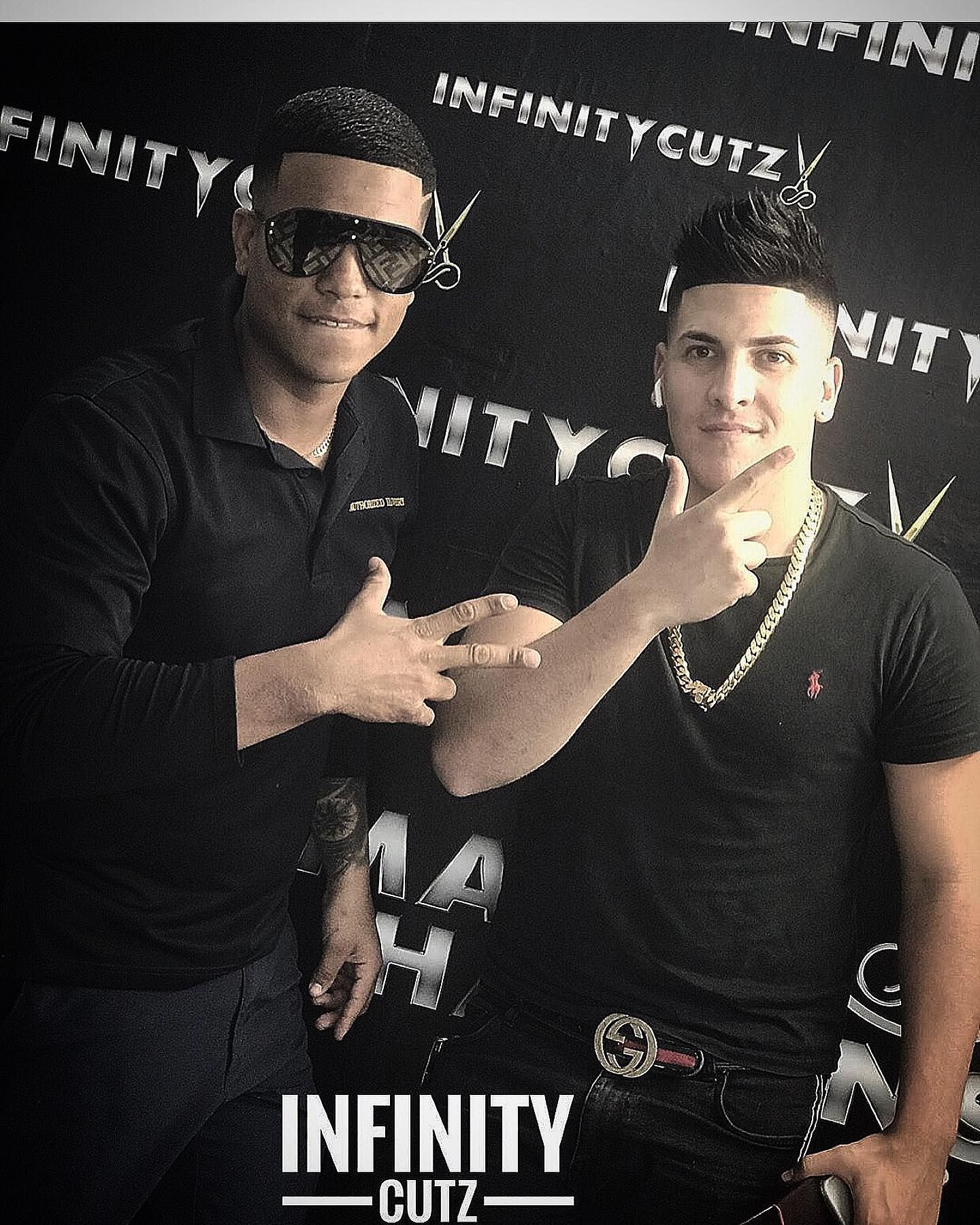 Two men are posing for a picture in front of a sign that says infinity cutz