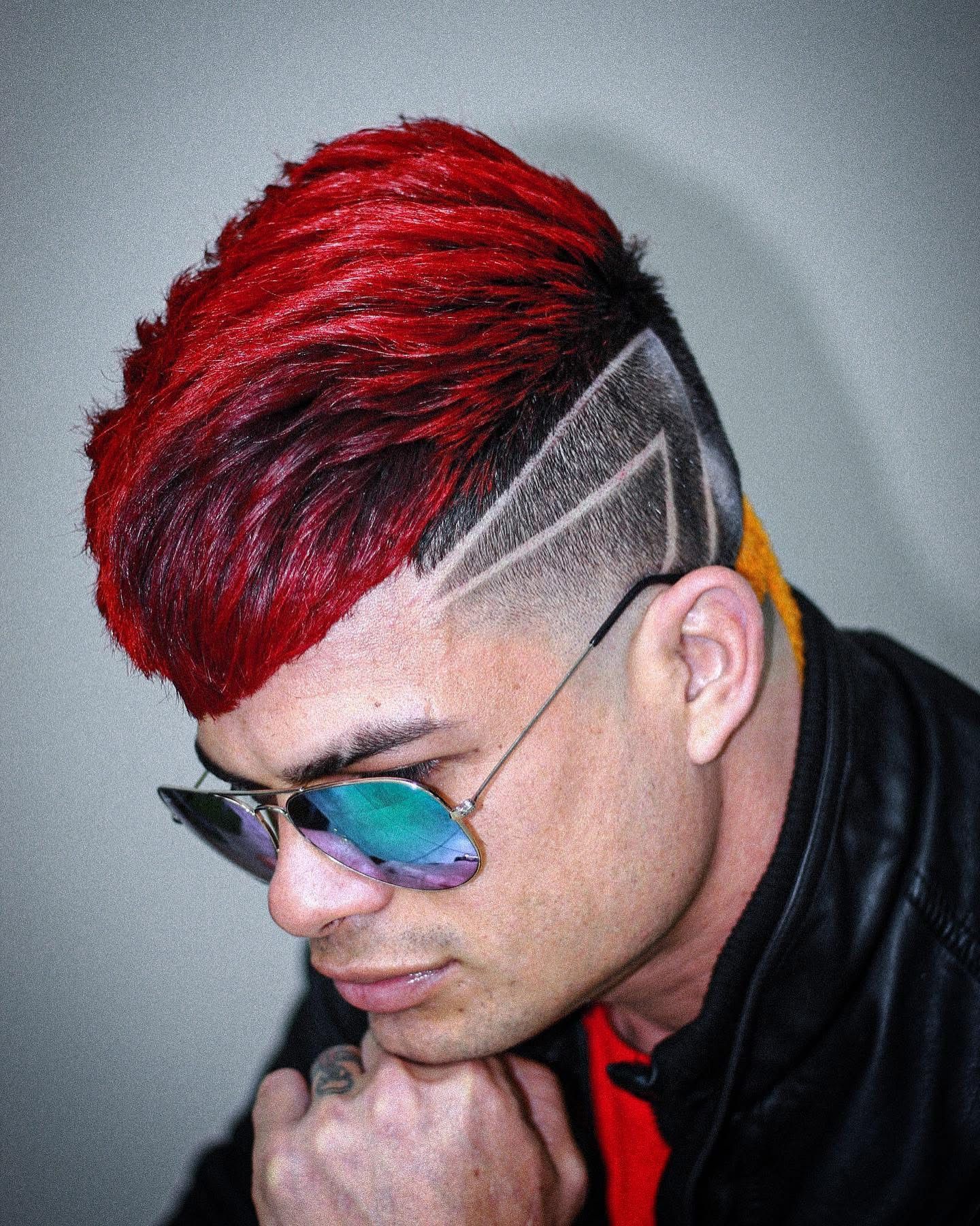 A man with red hair and sunglasses is wearing a black jacket.