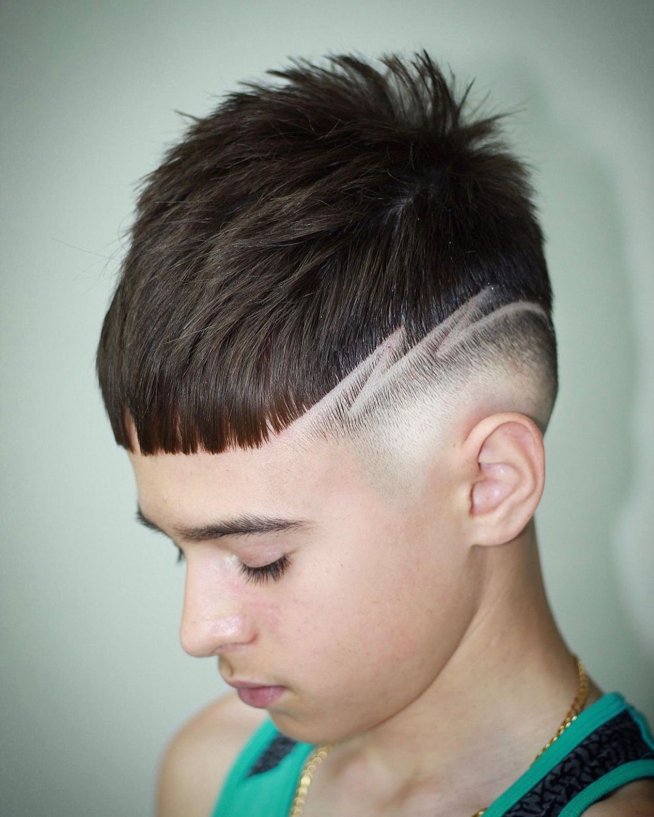 A young boy with a shaved design in his hair is wearing a green tank top.