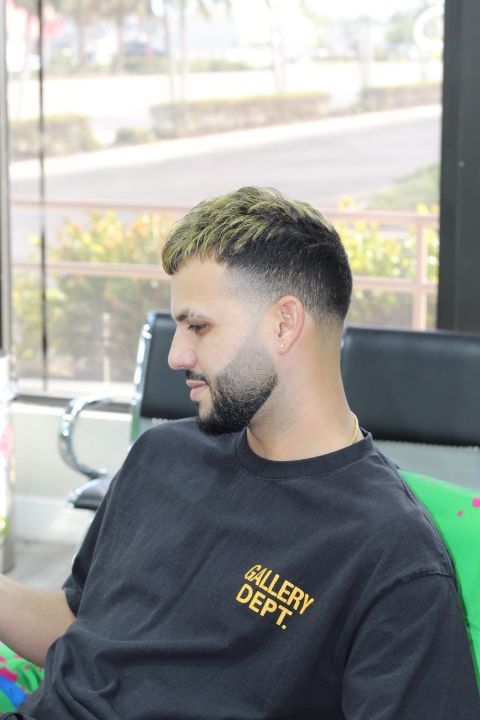 A man with a beard and a black shirt is sitting in a chair.