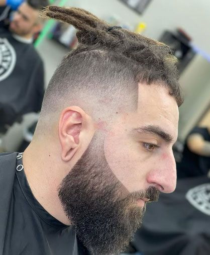 A man with dreadlocks and a beard is getting his hair cut at a barber shop.