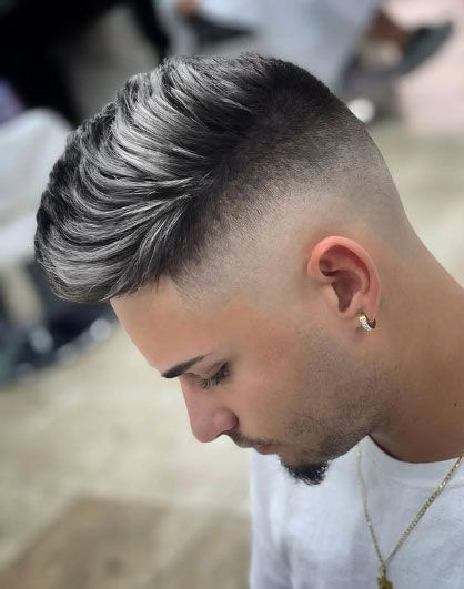 A man with a fade haircut is wearing a white shirt and earrings.