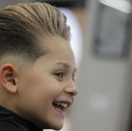 A young boy is smiling while getting his hair cut at a barber shop.