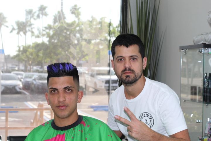 A man with purple hair is getting his hair cut by a barber.