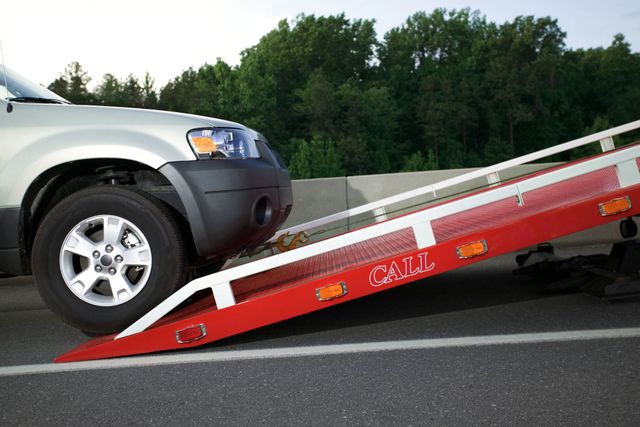 A silver car on a red tow truck ramp on a paved road, likely for transport.