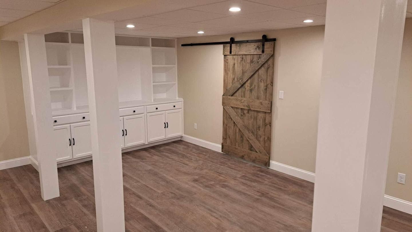 Basement room with wood floor, built-in white shelving, and a rustic barn door.